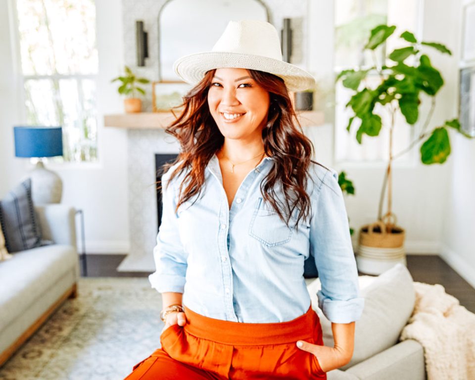 Anita, smiling in her living room with her hands in her pockets