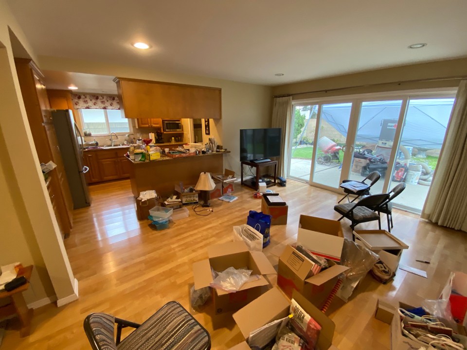 Before photo of a living room with sliding doors, and a small, dark kitchen in the back corner