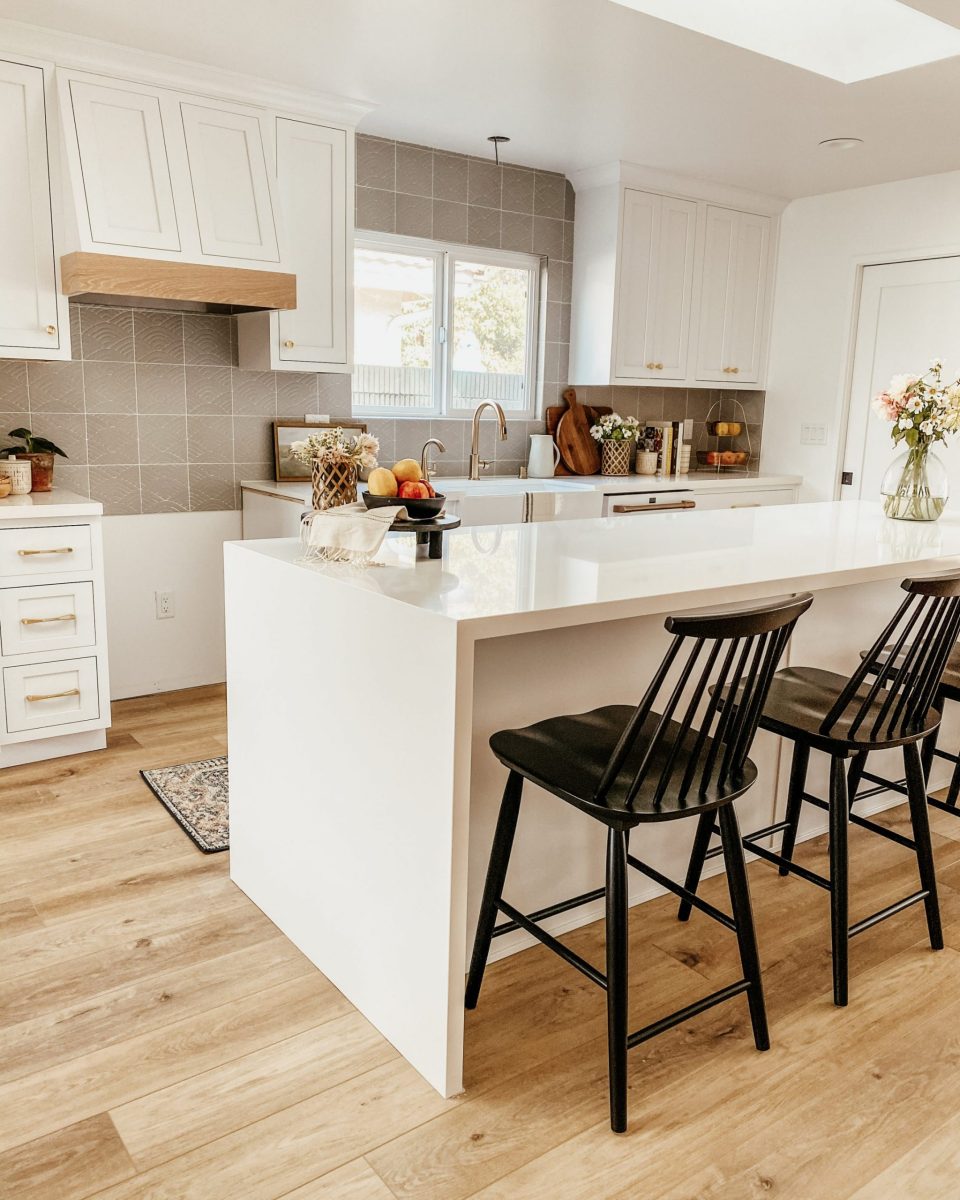 Waterfall style island with white countertops in a bright, clean, minimalist kitchen