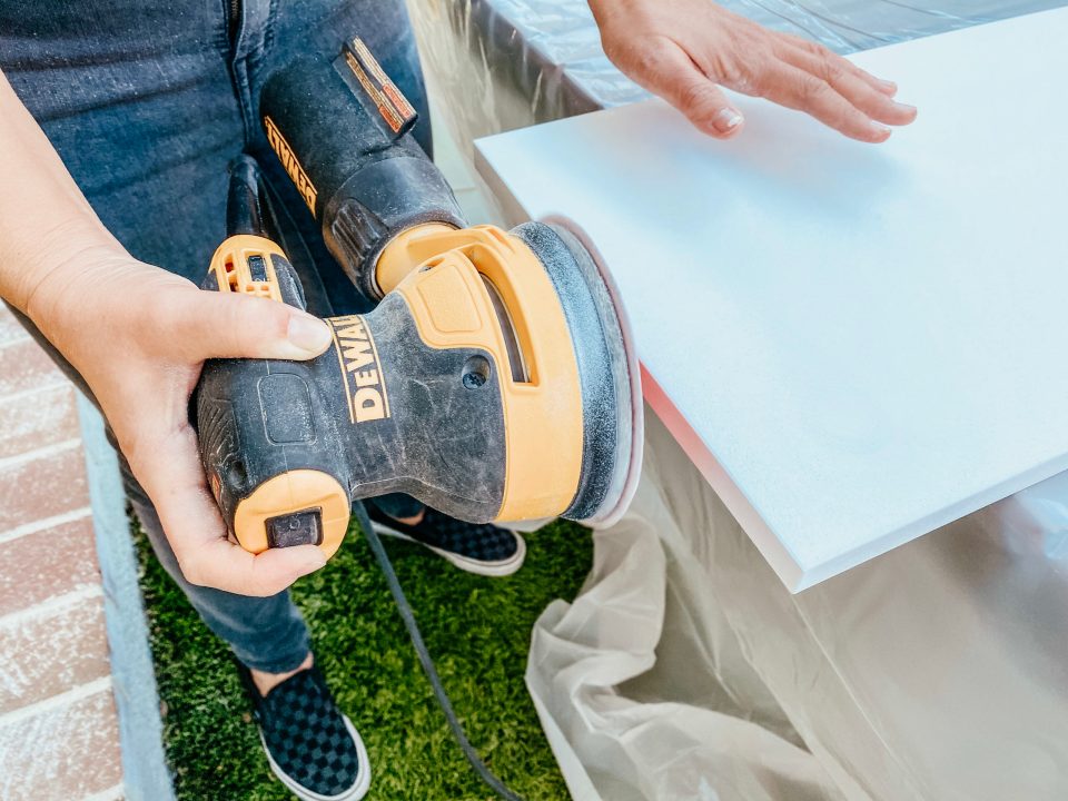 Anita takes a power sander to the edges of the melamine cabinet