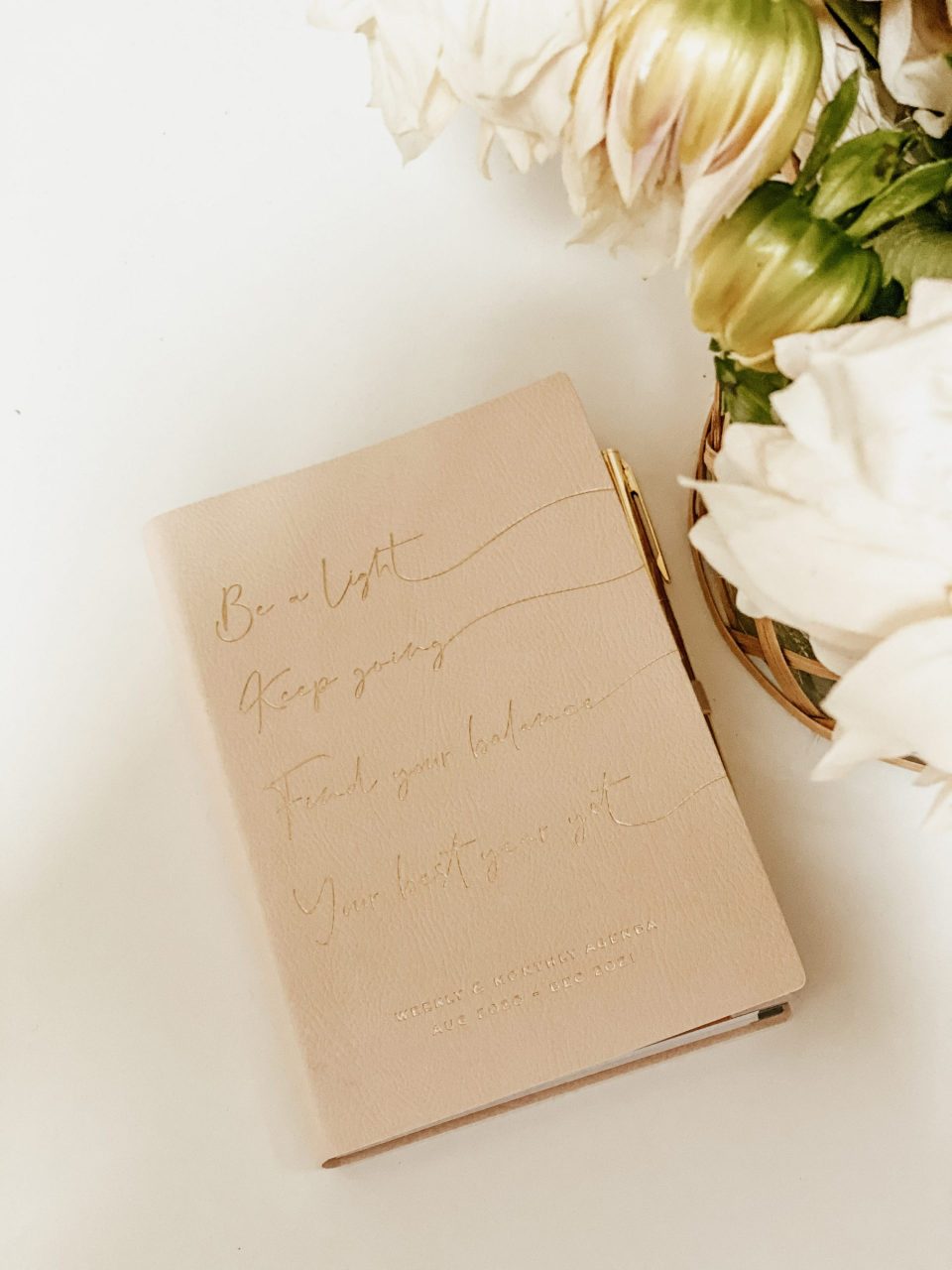Planner next to flowers on a clean, white desk