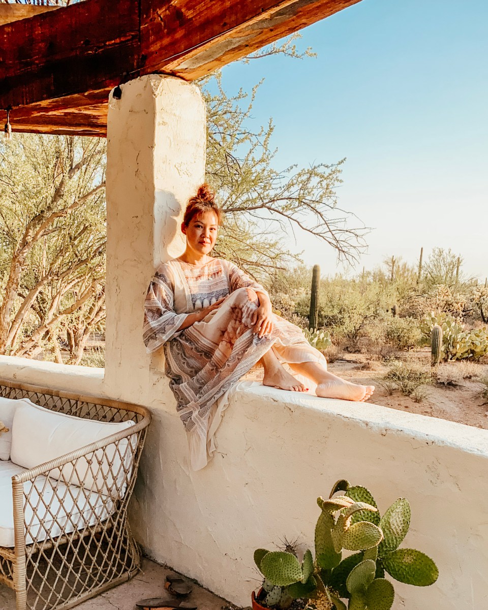 Anita sits on a low wall in the Arizona desert, looking into the camera