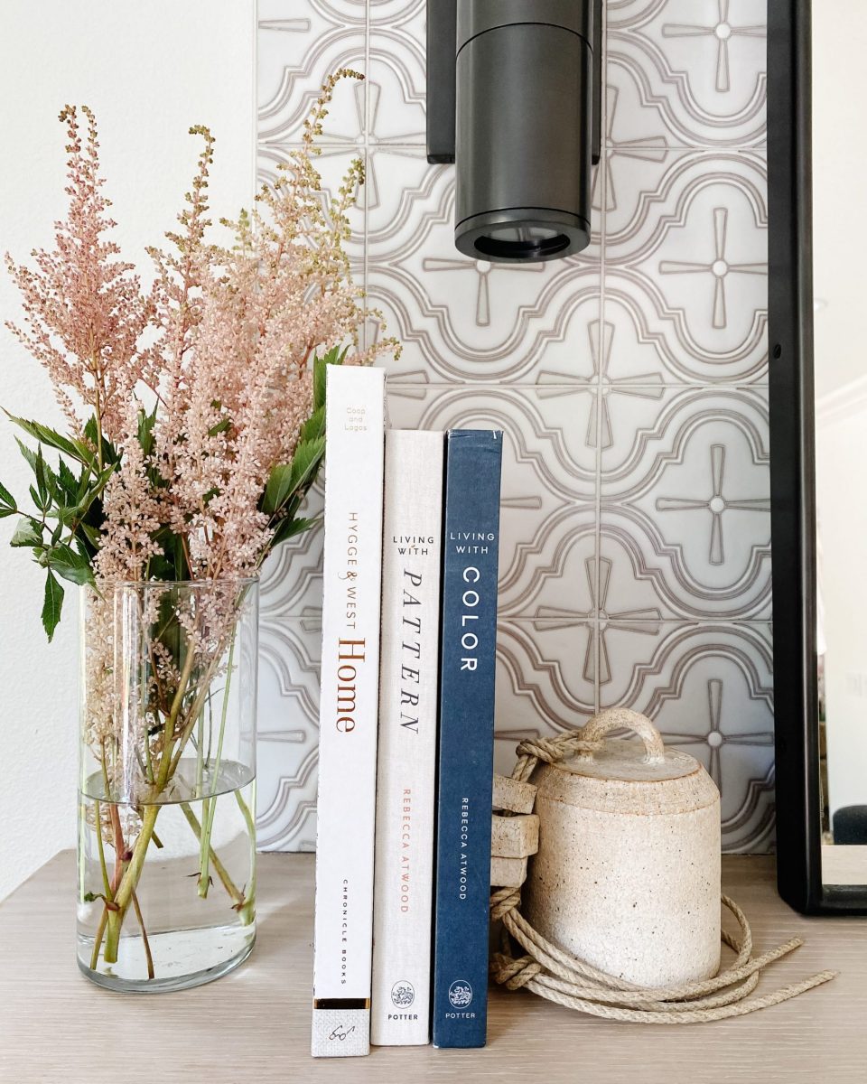 Books arranged on the mantle with flower arrangement and soft, patterned tile
