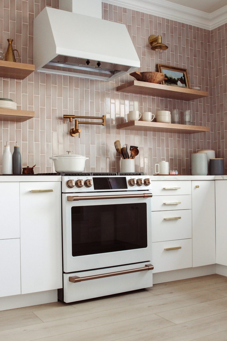 A white stove set in white modular cabinets with brass hardware against mauve backsplash that goes all the way to the ceiling!